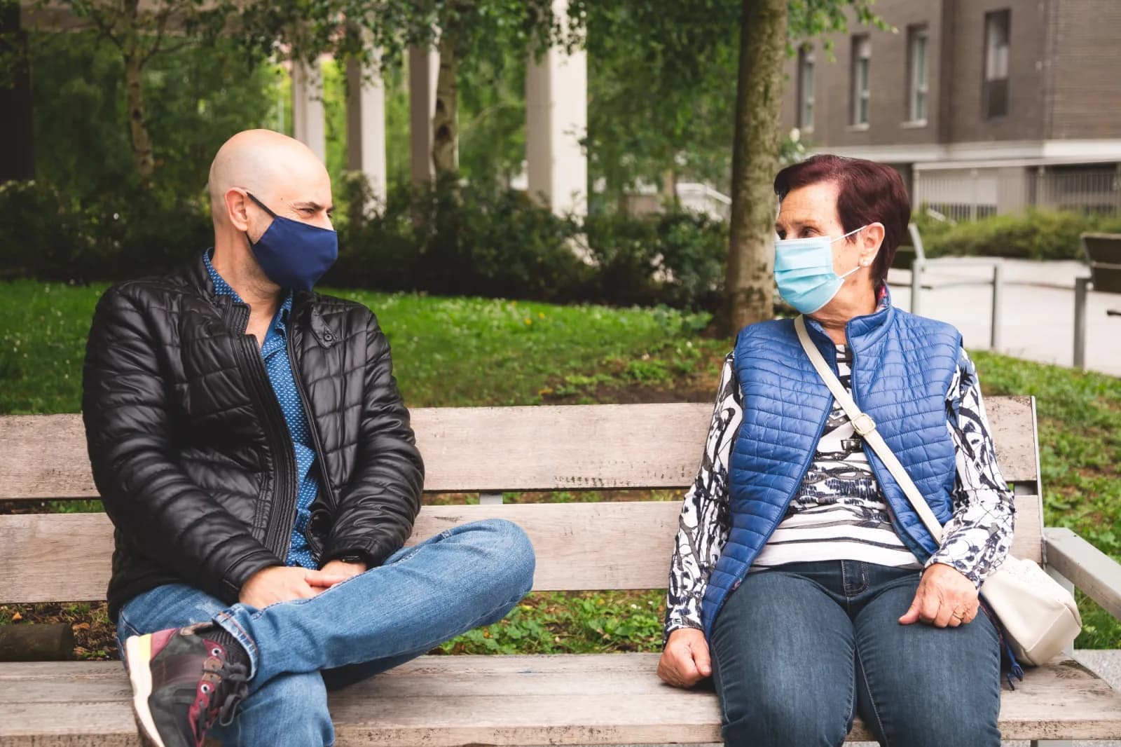 Man and older woman sitting on bench wearing face masks