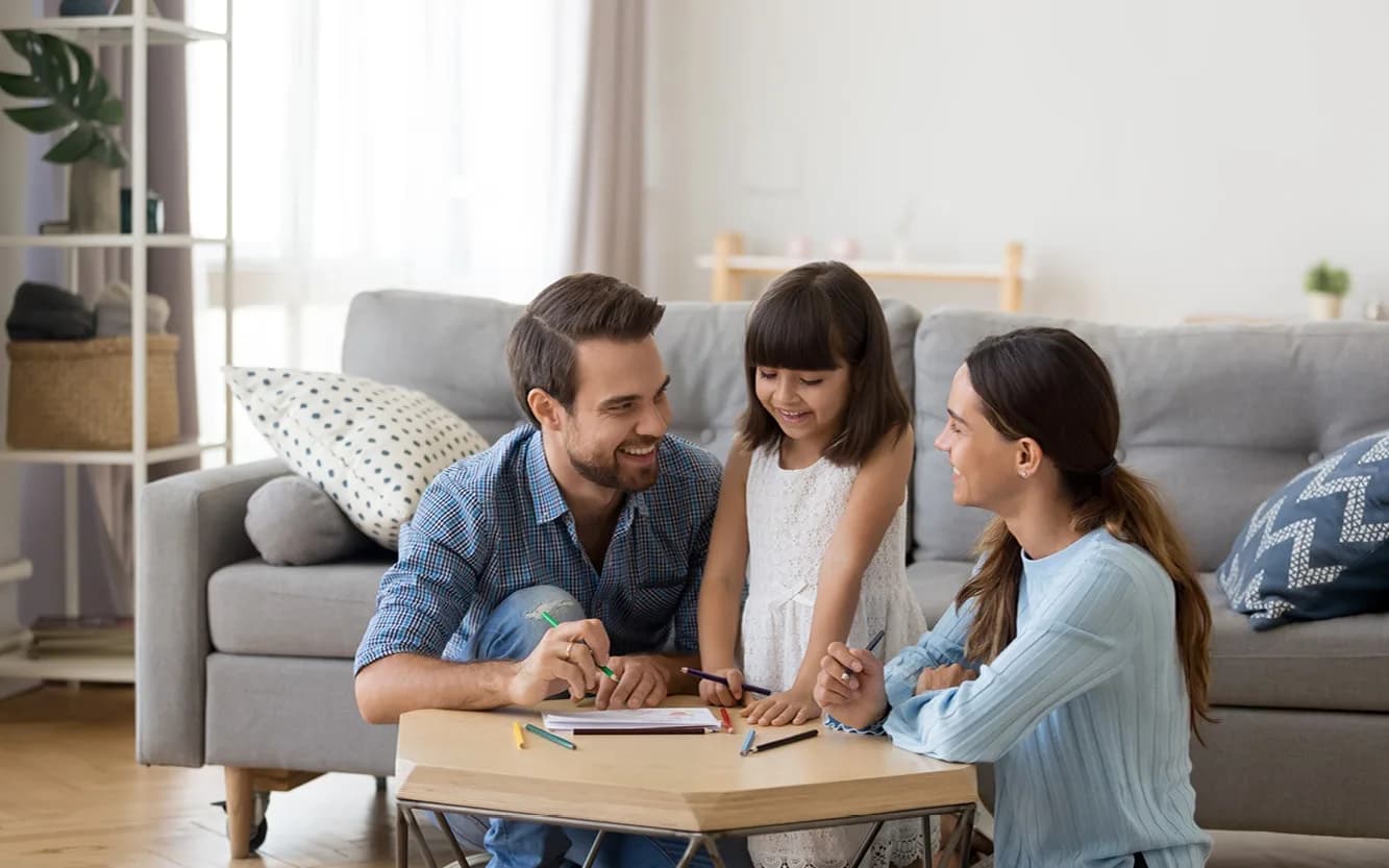 Young family of three smiling around coffee table