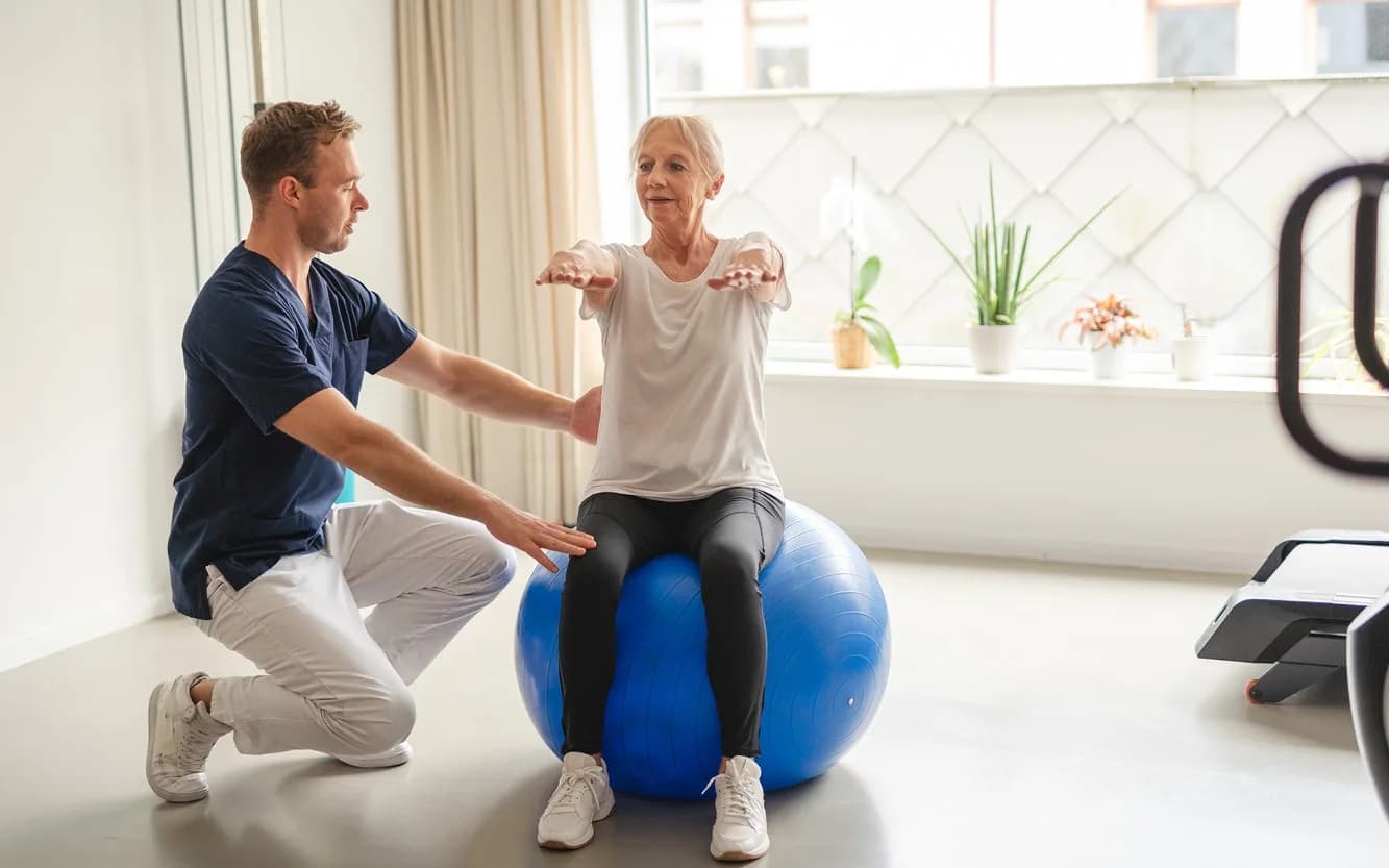 Physiotherapist helping patient with balance on a gym ball