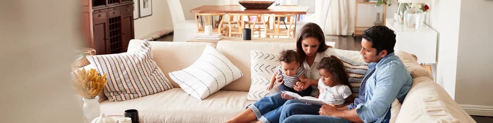 Family of 4 sitting on couch in living room looking at book